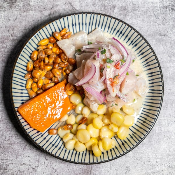 Peruvian ceviche with fish, red onion, corn, and sweet potato on a striped plate.