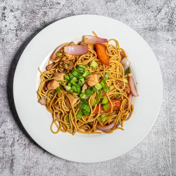 A white plate of Lomo Saltado with noodles, chicken, red onions, tomatoes, and green onions.