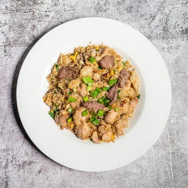 A white plate filled with fried rice, chicken, beef, and green onions on a gray background.