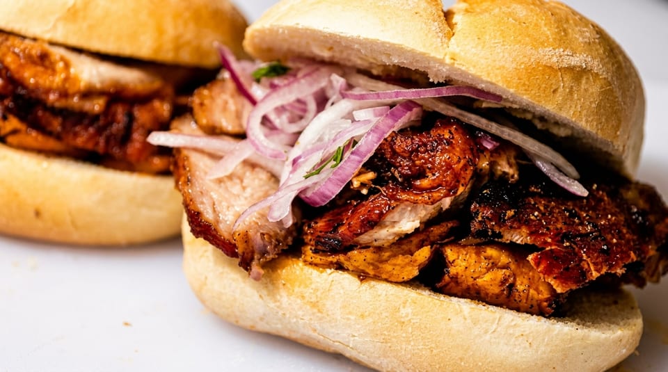 Two pork sandwiches on buns, topped with red onion slices and cilantro.