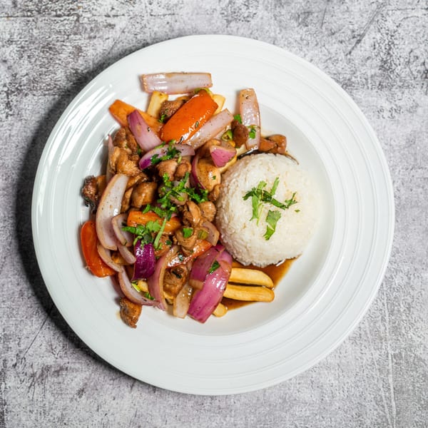Lomo Saltado with chicken, red onions, tomatoes, french fries, and white rice on a white plate.